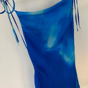 Blå klänning  - Blå klänning från asos design. Endast testad hemma då den är för stor för mig. Köptes sommaren 2023. Ryggen är öppen och man knyter vid axlarna så det känns bekvämt. Bilden på hemsidan visar en annan färg men klänningen är mer lik den första färgen. 