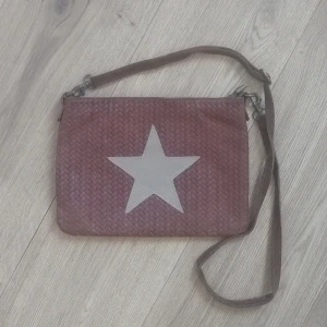 Läderväska  - Handväska / axelväska i läder. Stjärnmotiv. Bredd 27, höjd 21, axelband 105 på bild men justerbart. Lite slitningar på baksidan (sidan som är mot kroppen) annars bra. Mer mörkbrun än bilderna visar. 