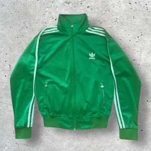 Adidas zipup grön - En snygg zipup från Adidas i fint skick. Knappt använd. 100% bomull. Står storlek XL på tagen men passar som S. Kontakta mig för mått!