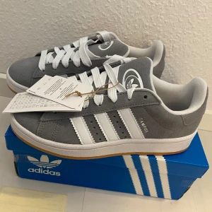 Nya Adidas Campus 00s -storlek 38 2/3 - Adidas Originals Campus 00 s j Storlek: 38 2/3.  Färg: Grey Three / Cloud White / Cloud White.  Ingår både vita och gråa skosnören.  Nya och oanvända. Köpta i Sverige och 100% äkta!