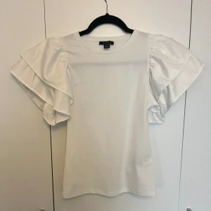Volang T-shirt  - En vit T-shirt med volang ärmar. Använd 1 gång. Väldigt söt, passar till alla tillfällen😇🤍