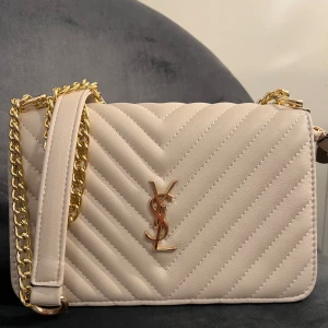 YSL väska - Fin beige väska med guldiga detaljer (fejk) säljer väskan då den aldrig kommit till använding. Den är som ny! Kom privat för fler bilder! 
