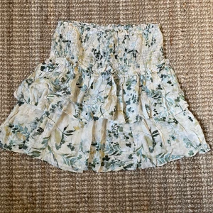 Volangkjol KappAhl - En jättefin gräddvit volangkjol från KappAhl som är i väldigt bra skick. Väldigt fina mörkgröna, ljusgröna och lite gult och blåaktiga detaljer. Dessutom skönt material och jättenajs på sommaren. Skriv för fler bilder💕💕