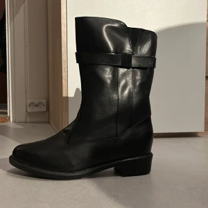 Svarta stövlar  - Svart stövlar i glansigt material och fint skick, har knappt tecken på användning. Är fodrade så passar jättebra under vintern. 