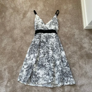 Klänning  - Vit klänning med svarta blommor på, regleringsbara axelband och band under brösten🤍🖤