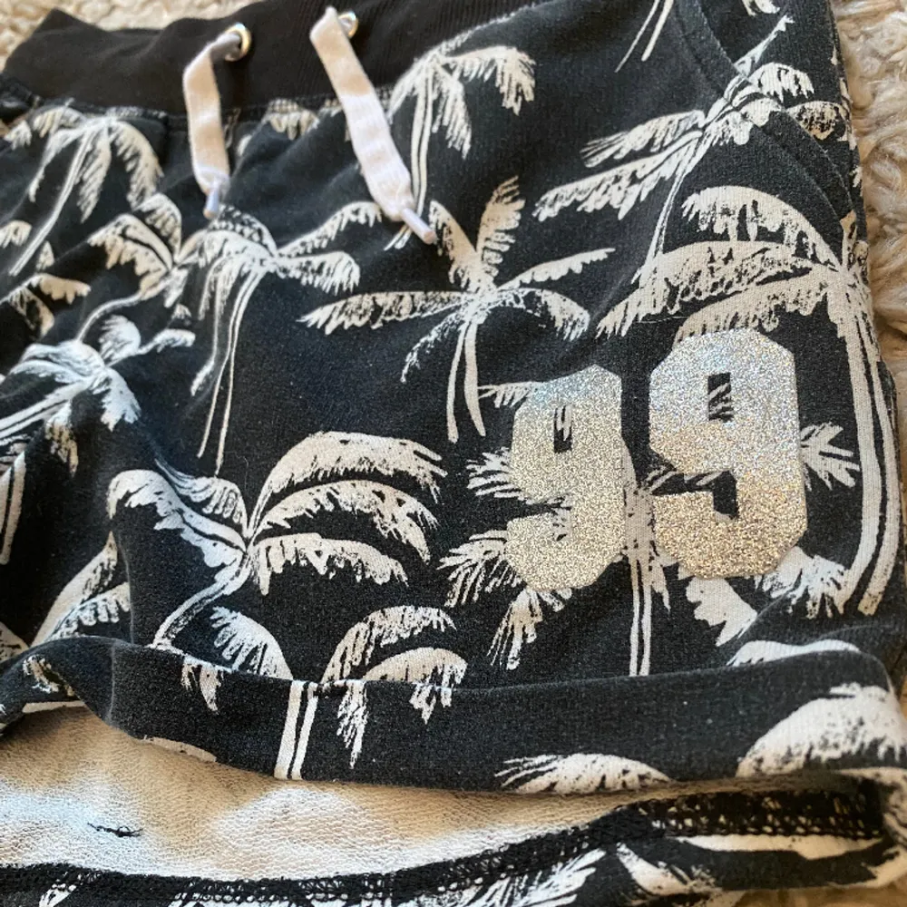 Svarta shorts med vita palmer på och 99 i silvrigt glitter på vänstra benet🖤🤍. Shorts.