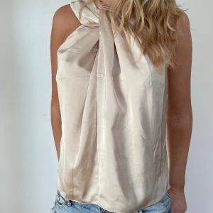 Topp - Beige/guldig topp i silkesimmitaton. Unik halsringning och jättemjukt material. Perfekt för festligare tillfällen! Bara att skriva om ni har några frågor💓