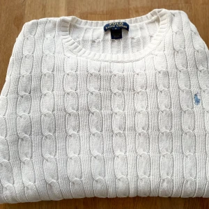 Ralph Lauren Stickad Tröja - Vit stickad Cable Knit tröja med blå logga. Storlek XL i ”Barn” storlek, passar som S. Tröjan är i mycket bra skick. Nypris är 2200kr. Pris går att diskutera.