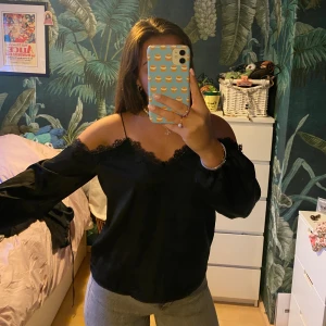 Svart blus - Söt långärmad blus med öppna axlar. Fin spets upptill och ganska stora ärmar som har en liten resor nertill. Jätteskön och luftig. Materialet är satinliknande.  Använd relativt många gånger men fortfarande som i nyskick.  Storlek S men passar även M.