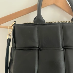 Svart väska - Svart väska med handtag samt justerbart axelband, gulddetalj. 