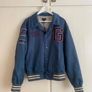 Blå bomberjacka från Gant - Blå/grönaktig bomberjacka från Gant. Muddarna är något noppriga och missfärgade.