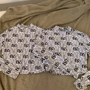 Vit långärmad tröja från FB Sister - Två vita långärmade tröjor från FB Sister med ett svart mönster. Tröjan har en hög krage och är lite magkort. Går att köpa ihop och separat. 1 för 50, 2 för 90kr