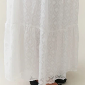 Vit långkjol - En elegant vit långkjol med ett subtilt mönster. Kjolen har en elastisk midja och är tillverkad i ett lätt och luftigt material, perfekt för varma dagar.
