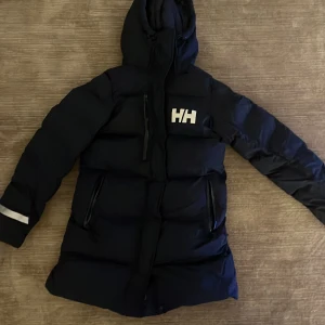 Helly Hansen damjacka - Jackan är i storlek XS (Junior) och köpt förra året, har endast använt i en vinter. Den är i god skick, inga skador eller missfärgningar. Ordinariepriset är 2600 kr. 