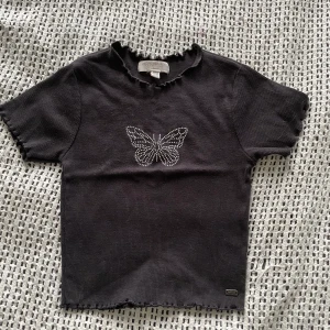 T-shirt med fjäril - Baby-tee med fjäril på av stenar. Knappt använd. Mörkgrå