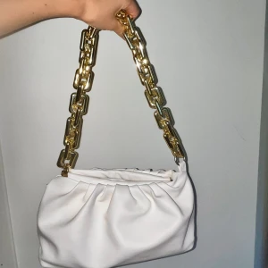 Vit och guldig axelväska - vit väska med guldig kedja, i bra skick, ena ögglan för bandet har låssnat men det är inget som man tänker på men därav det låga priset, nypris ca 300kr