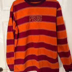 Tjockare långärmat tröja från Phug. Köpt i London för ca 500 kr. Oversized storlek M med randigmöster i orange, vinröd och gult. Tryck på framsida och baksida. Använd 1 gång. 