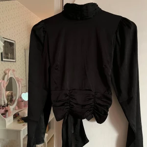 Blus med öppen rygg - En superfin svart långärmad blus med öppen rygg från Bubbleroom i strl 34!💓Tröjan har polokrage med knäppning baktill vid kragen samt knytning nedtill av tröjan!🫶🏻