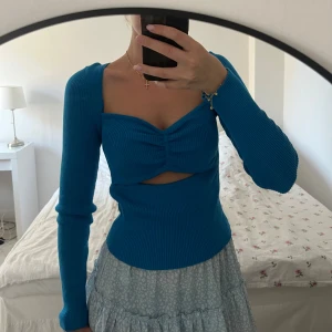Blå ribbad topp - En blå ribbad topp med långärmade ärmar och en knutdetalj framtill. Toppen har en åtsittande passform och en liten utskärning under bysten.