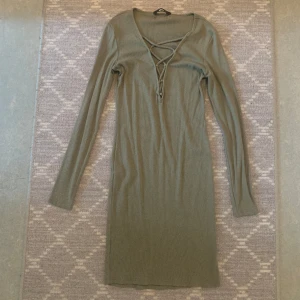 Tight Ribbad klänning  - Ribbad grön klänning med låg snörad urringning, storkel L, använd endast en gång.