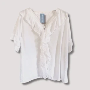 Fab Girl Blouse  - Söt blus med korta ärmar, volang längs framsida och i ärmslut. Fin att klä upp med klackar och kostymbyxa.  One size, passar upp till st. 42  Material: 85% Viskos 15% Polyamid  (Finns i beige och vit)  Vid intresse är det bara att höra av sig🌷