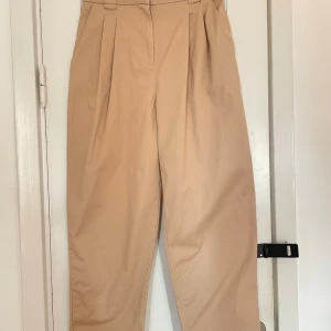 Kostymbyxor balloonleg  - Breda kostymbyxor med balloonleg och hög midja från H&M. Ljust beiga Rejäla i materialet. Stl 36 (S) Resår baktill Knäpps med två haspar, en knapp samt dragkedja i gylf.  Finns ett litet märke efter ett skärp annars är dom i mycket fint skick!