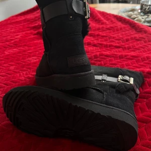 Svarta UGG med spännen  - Storlek 38 ( upplevs mindre i storleken ) Hel ny, aldrig använt. 