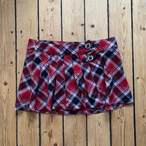 Rutig minikjol - Rutig lågmidjad minikjol, lite slitningar vid spännena. Midjemått 41cm, längd 32cm. Justerbart med spännen