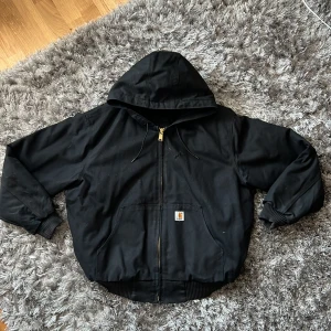 Carhartt Hooded Jacket - Rejäl fodrad jacka från Carhartt, perfekt vinterjacka. En lagning på på framsidan som är cirka 2cm stort. Boxy fit.  Mått: 70 cm på bredden 79 cm på längden 64 cm ärmlängd