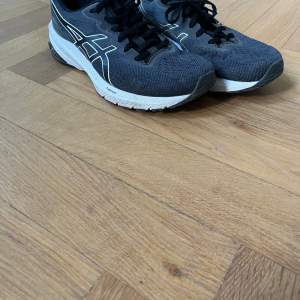 Ett par svarta Asics GT-1000 sneakers med vita detaljer och snörning. Skorna har en vit sula och är designade för löpning och träning.