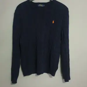 En mörkblå stickad tröja från Polo Ralph Lauren med ett orange broderat märke på bröstet. Tröjan har långa ärmar och en rund halsringning. Den är helt nytt använd två gånger gillade inte den och vi kan snacka om priset.