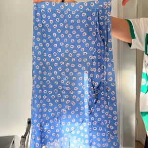 Blå blommig kjol - En blå långkjol med ett blommigt mönster. Kjolen har en volangdetalj längst ner och är tillverkad i ett lätt och flödande material.