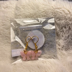 002. Nya guldfärgade örhänge med rosa fjärilar, nickelfria  - Till örhängena ingår små gummipluppar att sätta på baksidan så att örhängena sitter lite bättre på plats.  Örhängena är fint inpackade i en liten cellofanpåse med ett litet klistermärke på baksidan. Perfekt att ge bort som present.