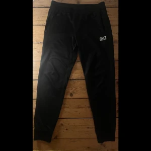 Svarta Armani trackbyxor - Svarta EA7 trackbyxor. Mycket bra kvalitet på dom, till skillnad från de flesta trackbyxorna är dessa mycket skönare för dem har bommulsmatrial på insidan som mjukisbyxor har. Sedan ett svart och glansigt material på utsidan. Mycket bra skick 10/10.