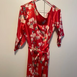 Blommig satin klänning - Off shoulder på en axel. Satin material. Band som man knyter runt midjan. Använd fåtal gånger. Från HannaliciousXnakd   Passar även en som har storlek 38