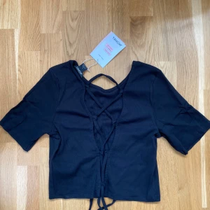 Tshirt med snörning  - Svart ribbar tshirt med öppet i ryggen med snörning. Superfin men har helt glömt bort den. Ny med lappkvar