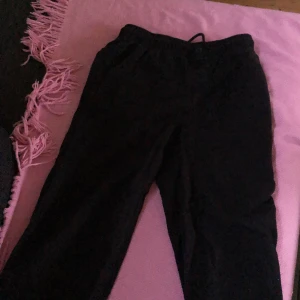 Svarta byxor från H&M med resårmidja - Svarta byxor från H&M med resår i midjan och två stora fickor framtill. Byxorna har en rak passform och är tillverkade i ett mjukt material som känns bekvämt. Perfekta för en avslappnad stil.