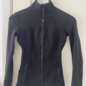 Svart träningsjacka från Lululemon - Säljer en svart, figursydd träningsjacka från Lululemon med dragkedja framtill och två fickor med dragkedja. Materialet Luon, kan även tänka mig byta mot en croped i annan färg!