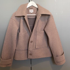 Beige kappa från Kappahl - Säljer en stilren beige kappa från Kappahl i storlek XS. Jackan har stora framfickor, bred krage och knäppning framtill med två knappar. Perfekt för dig som gillar klassisk och enkel design. Jätteskön och använd fåtal gånger 