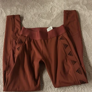 Röd bruna tights från Adidas - Säljer ett par röd bruna tights från Adidas med loggor längs sidorna. De har bred resår i midjan. Då de inte står vilken storlek skulle jag gissa 32-34 säljer dem för de inte kommer bli använda priset kan diskuteras💗