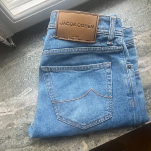Ljusblå jeans från Jacob Cohën - Säljer ett par ljusblå jeans från Jacob Cohën i modellen Bard som är en nyare modell än dom flesta har. Dem är i princip helt nya, använts under 5 gånger. Köptes på Ströms för 5000kr så allt tillbehör ingår. Storlek 30. 