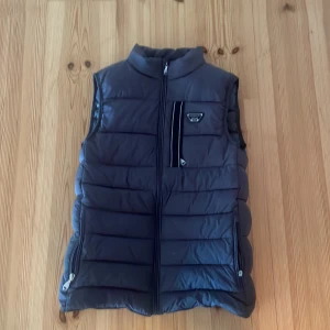 Svart dunväst från Alessandro - Snygg Alessandro’s väst säljer pga bytt still. Den har inga defekter alls förutom att dragen på en av fickorna är borta därefter pris. Han används väldigt lite.