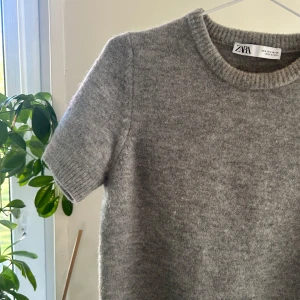 Grå stickad tröja från Zara - Mysig grå stickad tröja från Zara med korta ärmar och rund halsringning. 