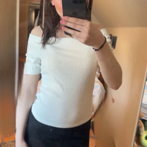Vit ribbad offshoulder topp - Säljer en vit ribbad topp med offshoulder-design och korta ärmar. Snygg och enkel modell som passar till mycket. Perfekt för dig som gillar stilrena plagg med en twist.