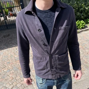 Svart overshirt - Säljer en svart overshirt från Uniqlo med tre stora fickor framtill och knäppning med fyra knappar. Jackan har klassisk krage och är tillverkad i bomull, perfekt för en stilren och avslappnad look. Storleken är xs men sitter som M