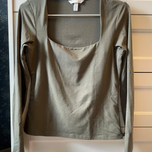 Olivgrön långärmad topp med fyrkantig ringning - Säljer en olivgrön långärmad topp med snygg fyrkantig ringning. Toppen är i mjukt material och har en enkel, stilren design som passar till mycket. Perfekt för dig som gillar minimalistisk stil.
