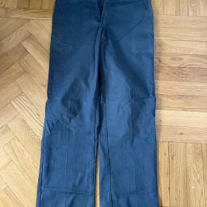 Mörkblå chinos Dickies - Snygga mörkblå chinos med rak passform och klassisk design. Byxorna har diskreta bakfickor med knapp och är perfekta för en stilren look. Passar till många olika tillfällen och är lätta att matcha med andra plagg.