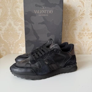 Valentino Garavani Rockrunner  - Säljer ett par svarta Valentino Garavani Rockrunner sneakers med kamouflagemönster. Skorna har snörning, rund tå och platt sula. Materialmix av mocka, skinn och textil ger en lyxig känsla. Perfekta för dig som vill ha något unikt och stilrent. Vid minsta funderingar så är det att höra av sig MVH CH