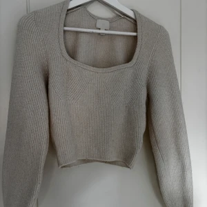 Beige stickad croppad tröja från H&M - Säljer en beige stickad tröja från H&M med fyrkantig ringning och croppad passform. Tröjan har långa ärmar och är perfekt för lager-på-lager-stil. Enkel och stilren design som passar till mycket.