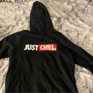 Svart hoodie med tryck från FSBN - Svart hoodie från FSBN med texten 'JUST CHILL.' tryckt på bröstet i vitt och rött. Klassisk huva med dragsko och stor magficka framtill. Perfekt för en avslappnad stil.